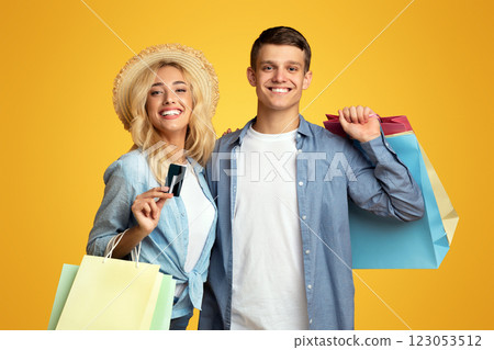 Travel shopping concept. Young couple of tourists with shopper bags and credit card on yellow studio background, copy space Travel shopping concept. Young couple of tourists with shopper bags and credit card on yellow studio background, copy space 123053512