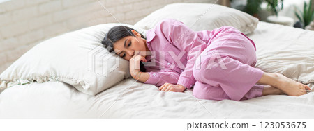 A young middle eastern woman in pink pajamas curls up on a soft bed, enjoying a peaceful sleep in her comfortable bedroom filled with natural light and gentle decor. 123053675