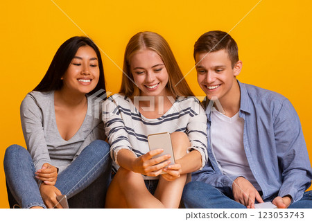 Group of multiracial classmates having break, watching videos on smartphone over yellow background Group of multiracial classmates having break, watching videos on smartphone over yellow background 123053743