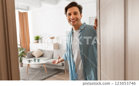 Portrait of cheerful man welcoming inviting visitor to enter his home, happy young guy standing in doorway of modern apartment, millennial male holding door looking out showing living room with hand Portrait of cheerful man welcoming inviting visitor to enter his home, happy young guy standing in doorway of modern apartment, millennial male holding door looking out showing living room with hand 123053746
