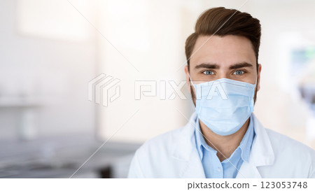 Closeup portrait of male doctor in protective face mask posing over clinic background, panorama with copy space. Young man dentist making treatment during coronavirus pandemic Closeup portrait of male doctor in protective face mask posing over clinic background, panorama with copy space. Young man dentist making treatment during coronavirus pandemic 123053748