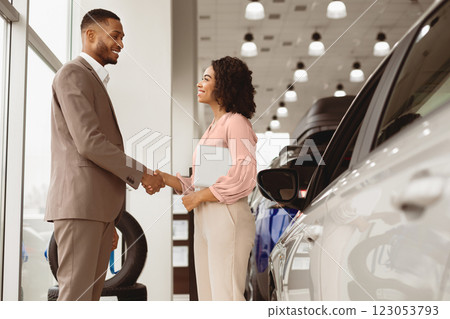 Buying Car Concept. Afro Businessman Handshaking With Manager Girl Standing Near Auto In Automobile Dealership Shop. Free Space 123053793