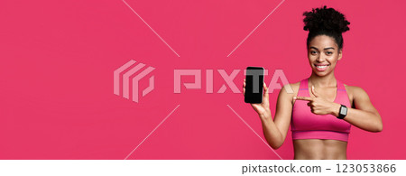 Trendy fitness mobile application. Sporty african american woman pointing at smartphone with blank screen and smiling over red background 123053866