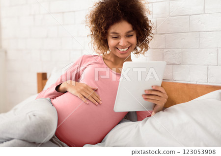 Pregnancy app. Happy afro woman using digital tablet and smiling, resting on bed Pregnancy app. Happy afro woman using digital tablet and smiling, resting on bed 123053908