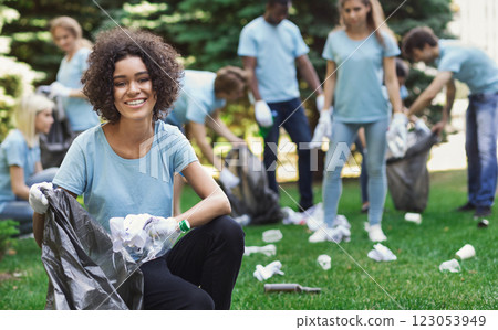 Volunteering, charity and clean environment concept. Happy black woman and group of volunteers with garbage bags cleaning area in park, copy space 123053949