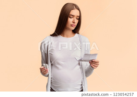 Pregnancy And Medication. Pregnant Lady Reading Instruction For Prescribed Pills Standing Over White Background. Studio Shot 123054257