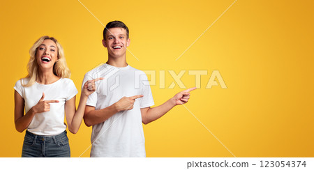 Joyful young guy and girl pointing away at copy space on yellow background 123054374