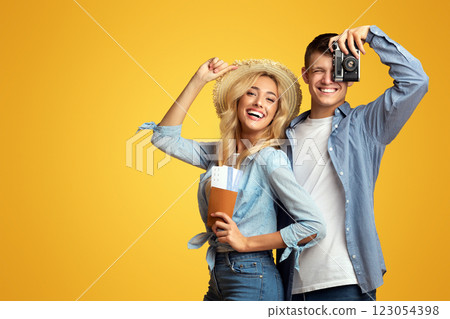 Ready for travel. Happy millennial couple holding passport with tickets and retro photocamera over yellow studio background with free space Ready for travel. Happy millennial couple holding passport with tickets and retro photocamera over yellow studio background with free space 123054398