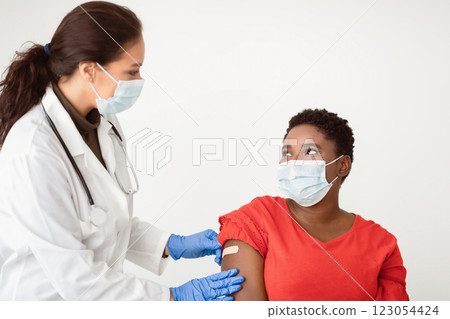 Antiviral Vaccination, immunization. African american female getting vaccine against Covid-19 for Coronavirus prevention. Medical worker sticking plaster bandage after injection on white background Antiviral Vaccination, immunization. African american female getting vaccine against Covid-19 for Coronavirus prevention. Medical worker sticking plaster bandage after injection on white background 123054424
