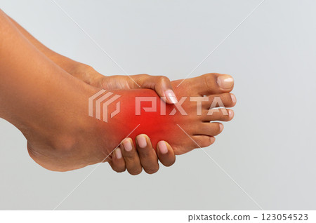 Cropped of black woman holding her painful foot, cramp, muscular spasm, red accent on sore zone 123054523