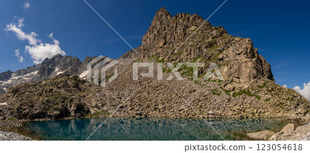 Clear mountain lake reflecting rugged cliffs and snow capped peaks in alpine landscape 123054618