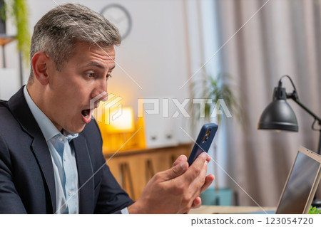 Happy amazed young Caucasian freelancer working on smartphone shocked by sudden victory at home 123054720