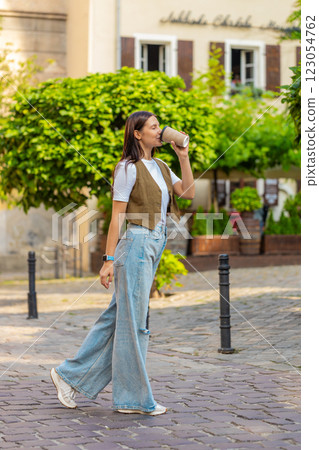 Happy Caucasian young pretty woman enjoying morning coffee hot drink and walking on city street 123054762