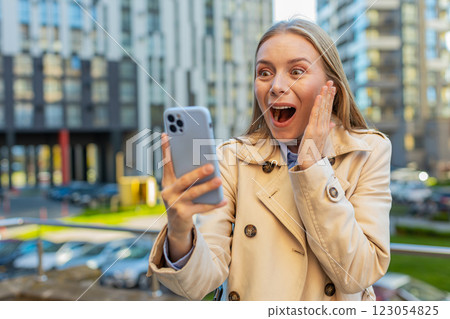 Caucasian mature woman looking shocked while reading good news on smartphone on downtown city street Caucasian mature woman looking shocked while reading good news on smartphone on downtown city street 123054825