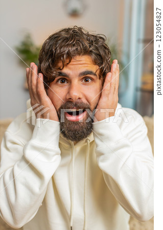 Wow emotion of bearded young Indian man surprised looking at camera with big eyes sitting on sofa 123054827