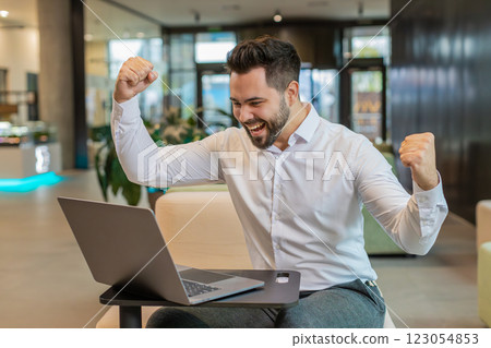 Caucasian bearded businessman working on laptop shocked by sudden victory in modern hotel lobby Caucasian bearded businessman working on laptop shocked by sudden victory in modern hotel lobby 123054853