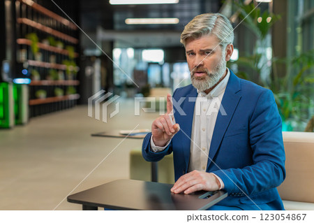 Serious mature businessman shakes finger and saying No be careful and giving advice in office lobby Serious mature businessman shakes finger and saying No be careful and giving advice in office lobby 123054867
