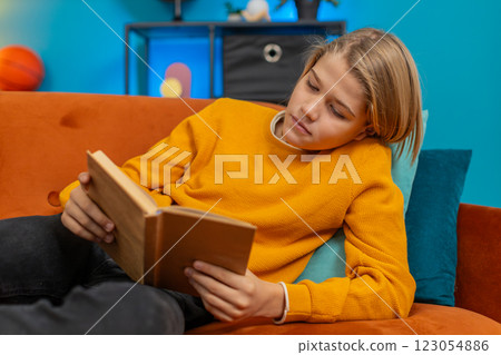 Teenager boy reading book, enthusiastically flipping pages, thoughtfully looking up, lying on sofa 123054886