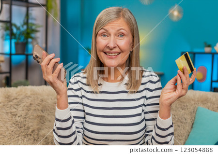 Mature woman shopping online on smartphone entering credit card info satisfied with purchase at home 123054888