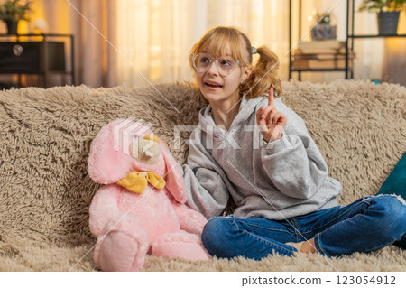 Young teenager child girl happily talking to plush bunny at home sofa pretend fun imaginative vibes Young teenager child girl happily talking to plush bunny at home sofa pretend fun imaginative vibes 123054912