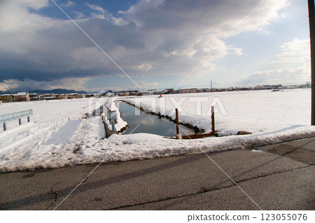 Afternoon sky and a waterway stretching across a snowy field 123055076