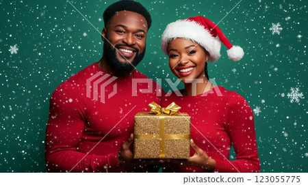 A cheerful couple dressed in red holiday attire smiles warmly at the camera while holding a beautifully wrapped gift. 123055775