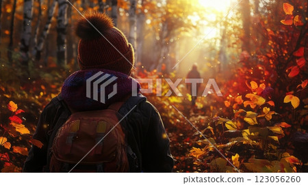 A person stands in an enchanting forest during autumn, surrounded by vibrant orange and yellow leaves. Sunlight filters through the trees, creating a magical atmosphere as another figure walks ahead. 123056260