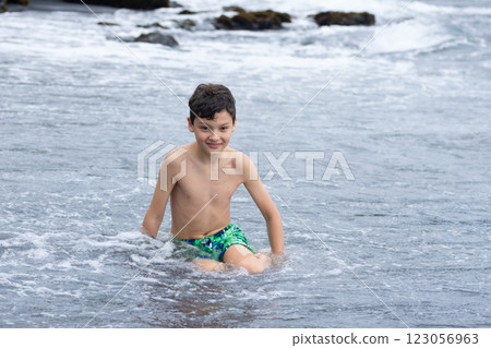 Teen boy is sitting on the Black sand beach in Hawaii. Teen boy is sitting on the Black sand beach in Hawaii. 123056963