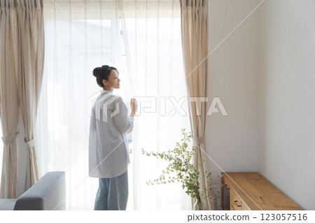 Woman opening curtains in living room 123057516