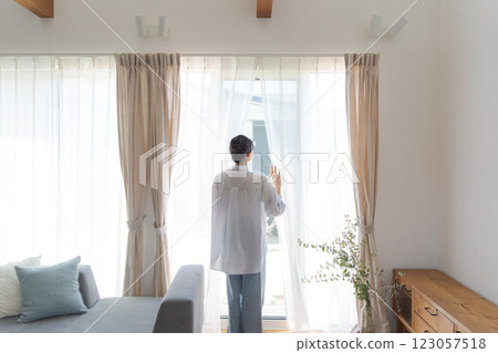 Woman opening curtains in living room 123057518