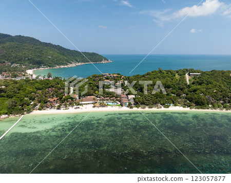 A small coastal village nestled in vibrant greenery with the turquoise sea in the background under a clear sky. Ko Pha Ngan, Thailand. A small coastal village nestled in vibrant greenery with the turquoise sea in the background under a clear sky. Ko Pha Ngan, Thailand. 123057877