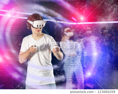 In darkened hall of gaming club, guy in VR helmet takes part in group game, visual special effects 123060209