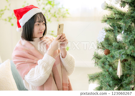 A woman taking a photo with her smartphone in front of a Christmas tree A woman taking a photo with her smartphone in front of a Christmas tree 123060267