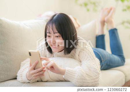 A young woman lying on a sofa and looking at her smartphone A young woman lying on a sofa and looking at her smartphone 123060272