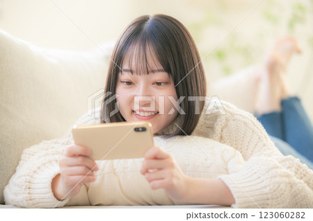 A young woman lying on a sofa and looking at her smartphone A young woman lying on a sofa and looking at her smartphone 123060282