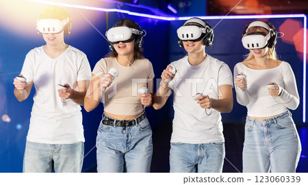 In darkened hall of gaming club, four friends in VR helmet takes part in group game In darkened hall of gaming club, four friends in VR helmet takes part in group game 123060339
