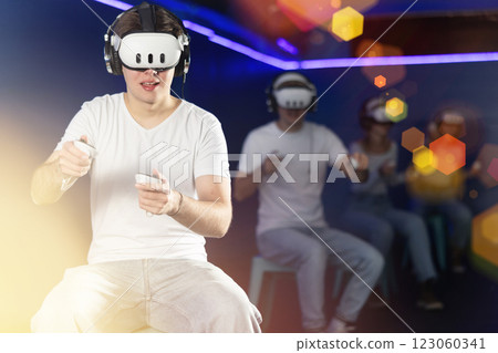 In darkened hall of gaming club, guy in VR helmet takes part in group game 123060341