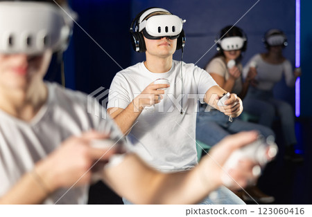 In darkened hall of gaming club, guy in VR helmet takes part in group game In darkened hall of gaming club, guy in VR helmet takes part in group game 123060416