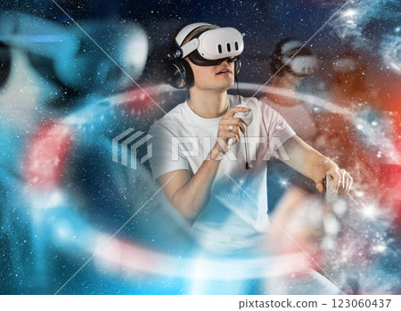 In darkened hall of gaming club, guy in VR helmet takes part in group game, visual special effects 123060437