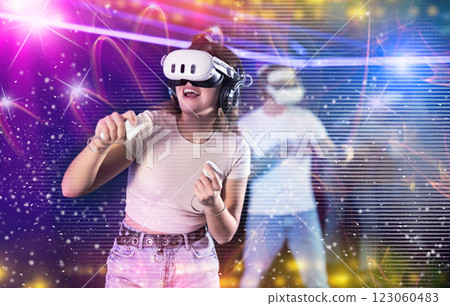 In darkened hall of gaming club, girl in VR helmet takes part in group game, visual special effects In darkened hall of gaming club, girl in VR helmet takes part in group game, visual special effects 123060483