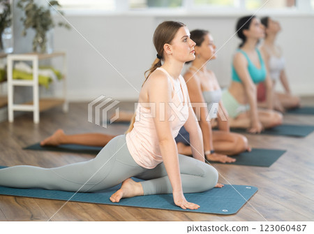 Young girl teaches yoga lesson, shows students technique of performing kapotasana asana Young girl teaches yoga lesson, shows students technique of performing kapotasana asana 123060487