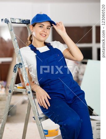 Positive builder woman in blue overalls next to stepladder 123060520