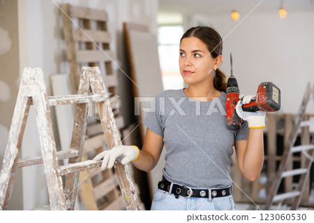 Smiling woman holding drill, repair works in apartment Smiling woman holding drill, repair works in apartment 123060530