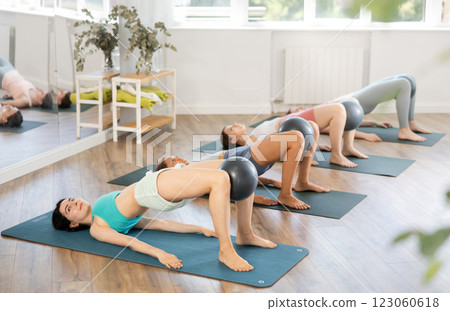 Together with students, she lies on mat, holds fitball between knees and raises and lowers buttocks 123060618