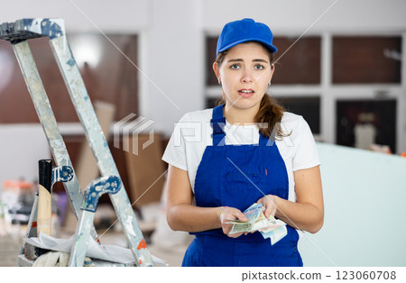Frustrated young workwoman with banknotes in hands at construction site 123060708