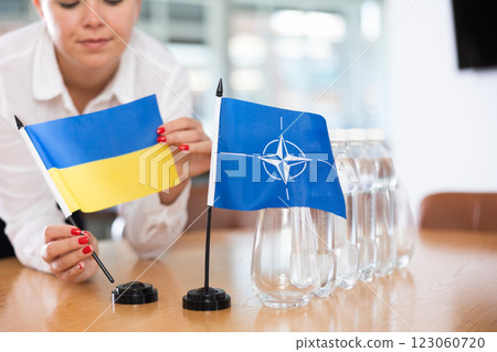 Young woman puts flags of Ukraine and NATO on table in office Young woman puts flags of Ukraine and NATO on table in office 123060720
