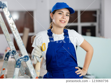 Positive young female builder in blue workwear standing at construction site 123060736