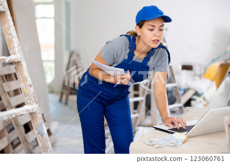 Portrait of a female builder who checks the work done using laptop 123060761