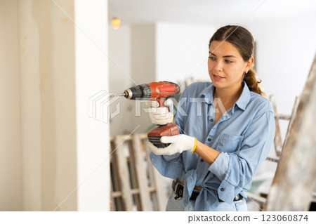 Woman builder using drill to bore hole in wall 123060874