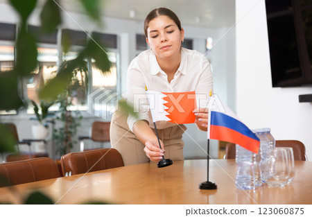 Preparing for business presentation - secretary places flags of Russia and Bahrain on negotiating table 123060875